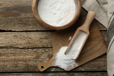 Baking powder in bowl and scoop on wooden table, flat lay. Space for text