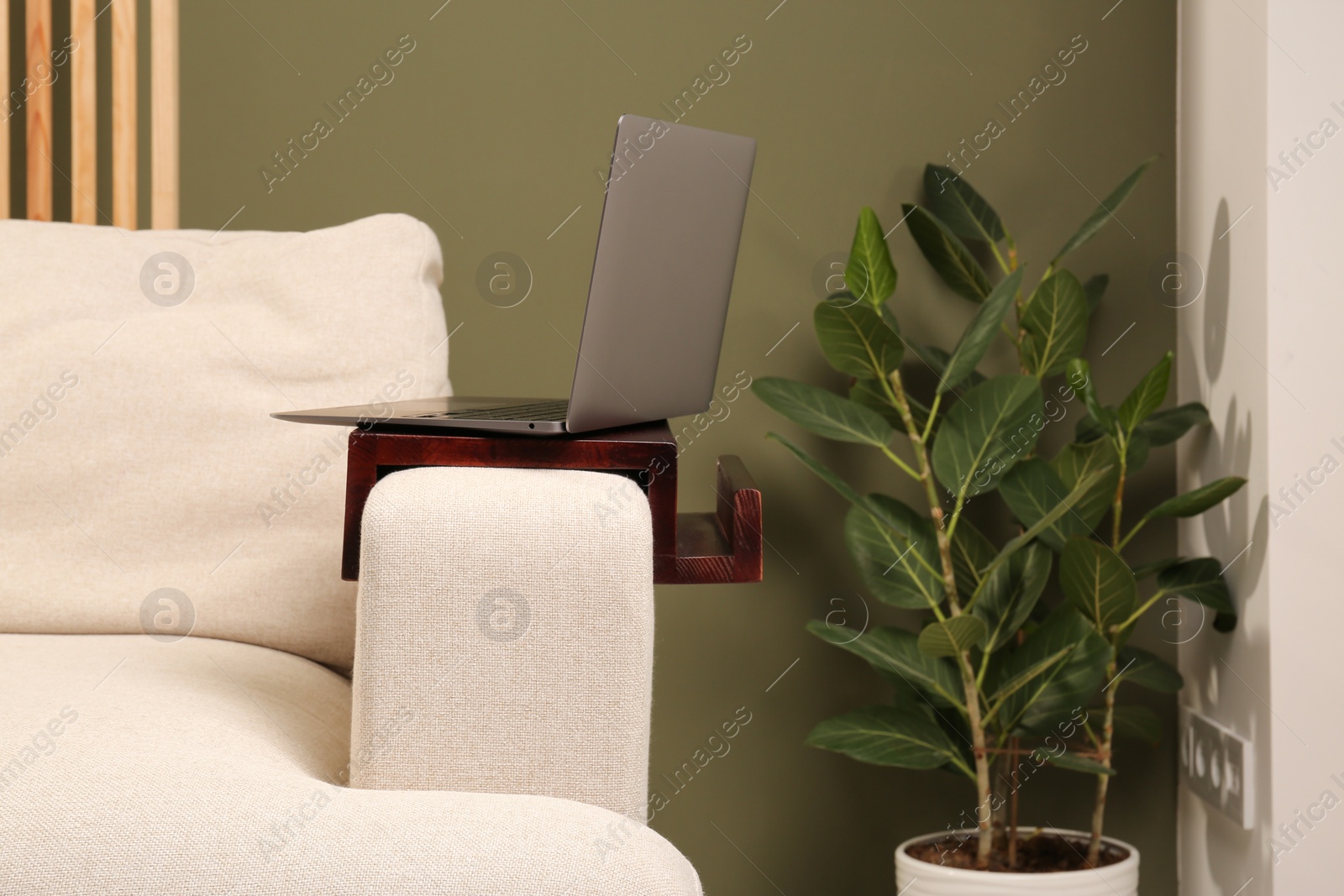 Photo of Laptop on sofa armrest wooden table in room. Interior element