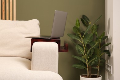 Laptop on sofa armrest wooden table in room. Interior element