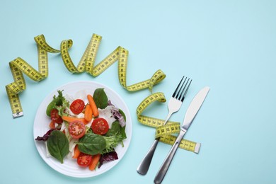 Measuring tape, vegetable salad and cutlery on light blue background, flat lay with space for text. Weight loss concept