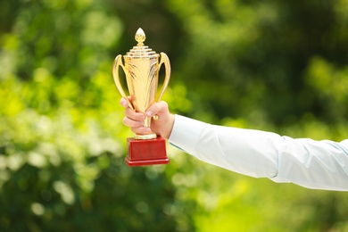 Photo of Young businessman holding gold trophy cup in green park, closeup