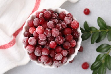 Frozen red cranberries in bowl and green leaves on light table, top view