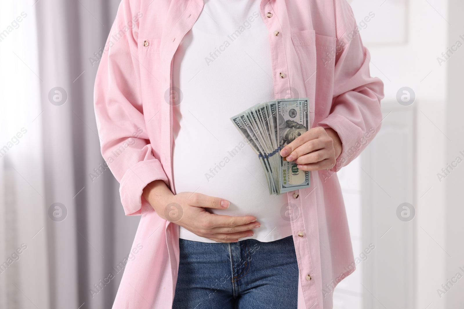 Photo of Surrogate mother. Pregnant woman with dollar banknotes indoors, closeup