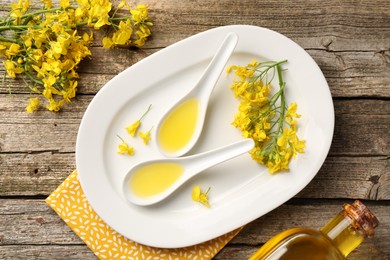 Photo of Rapeseed oil in gravy boats, bottle and beautiful yellow flowers on wooden table, flat lay