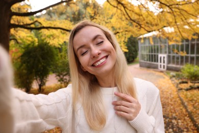 Photo of Portrait of happy woman taking selfie in autumn park