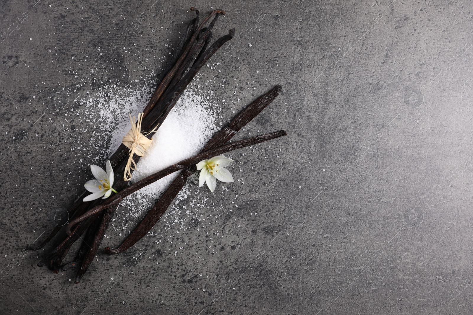 Photo of Vanilla pods, sugar and flowers on gray table, flat lay. Space for text