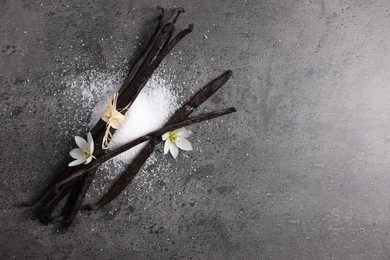 Photo of Vanilla pods, sugar and flowers on gray table, flat lay. Space for text