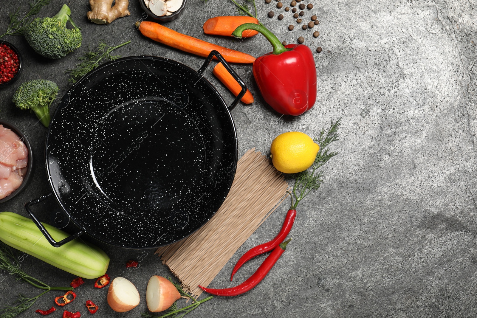 Photo of Empty iron wok surrounded by ingredients on grey table, flat lay. Space for text