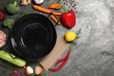 Empty iron wok surrounded by ingredients on grey table, flat lay. Space for text