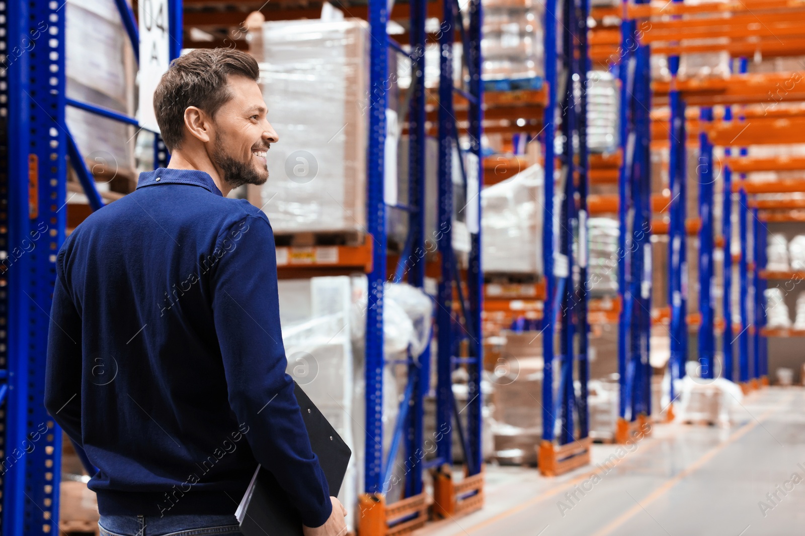 Photo of Happy manager holding clipboard in warehouse with lots of products. Space for text