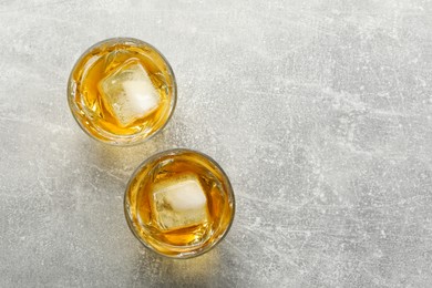 Photo of Tasty whiskey with ice in glasses on grey table, top view. Space for text