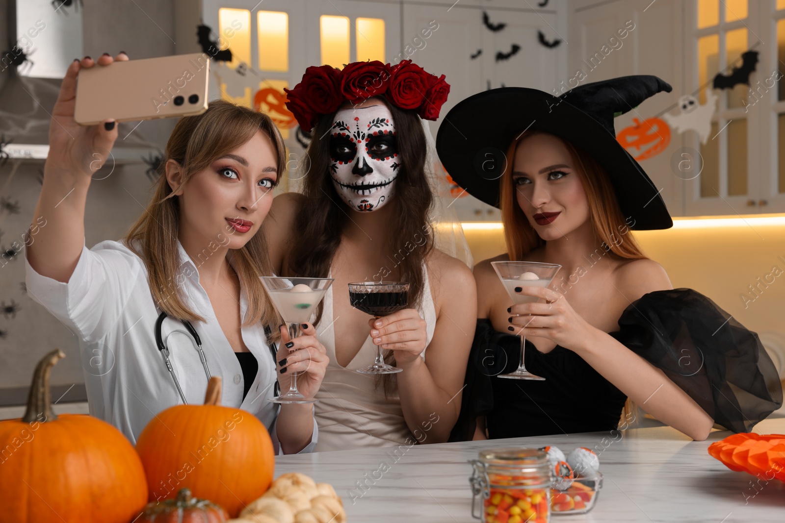 Photo of Group of women in scary costumes with cocktails taking selfie at Halloween party indoors