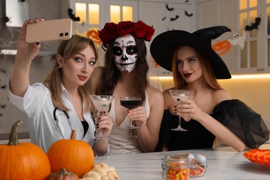 Group of women in scary costumes with cocktails taking selfie at Halloween party indoors