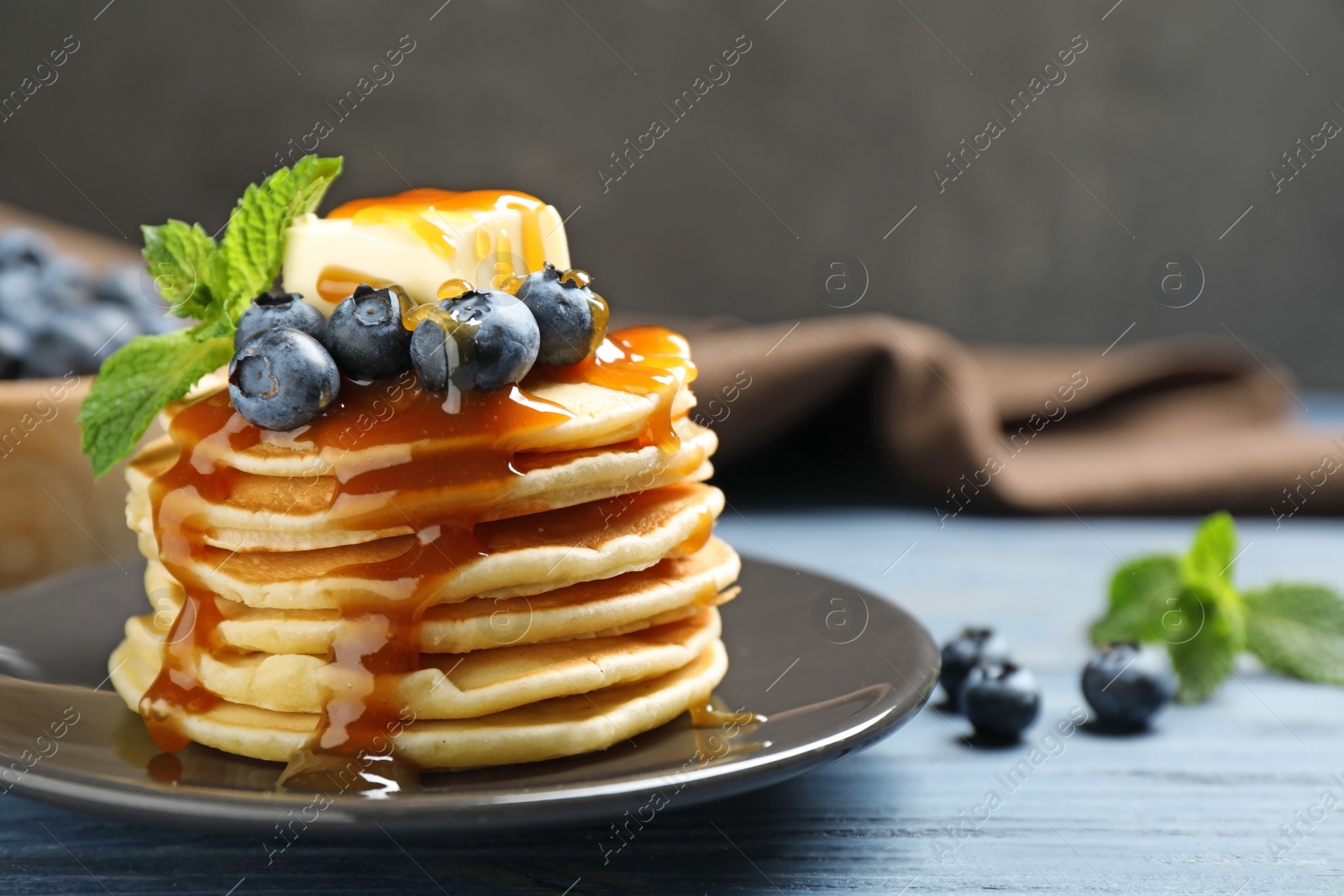 Photo of Delicious pancakes with fresh blueberries, butter and syrup on blue wooden table