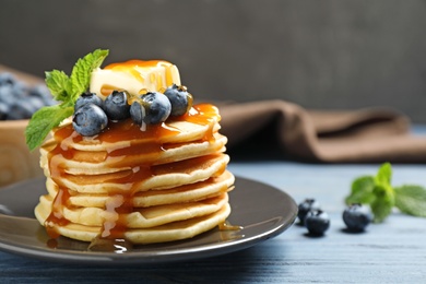 Delicious pancakes with fresh blueberries, butter and syrup on blue wooden table