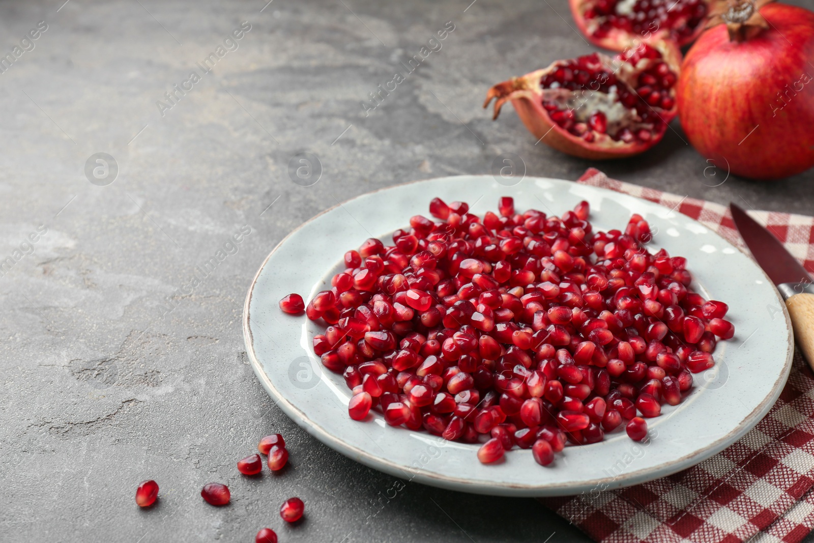 Photo of Tasty ripe pomegranate grains on grey table. Space for text