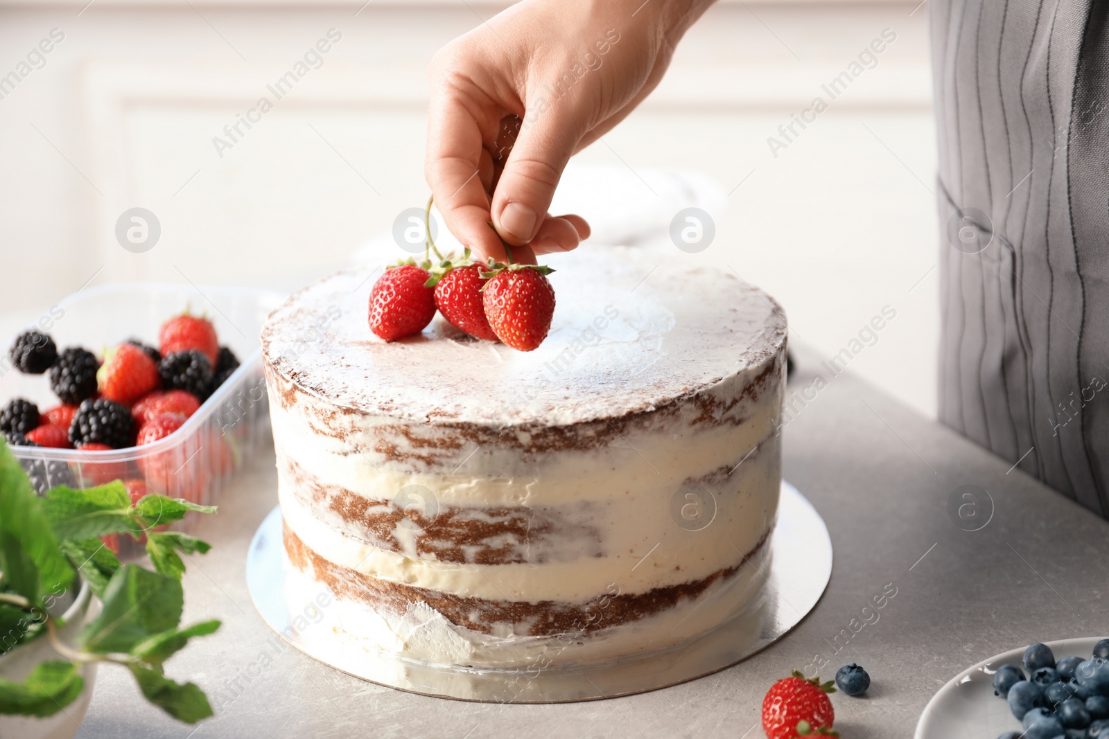 Photo of Woman decorating delicious cake with fresh berries at table. Homemade pastry