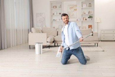 Photo of Happy man in headphones having fun with mop while cleaning at home