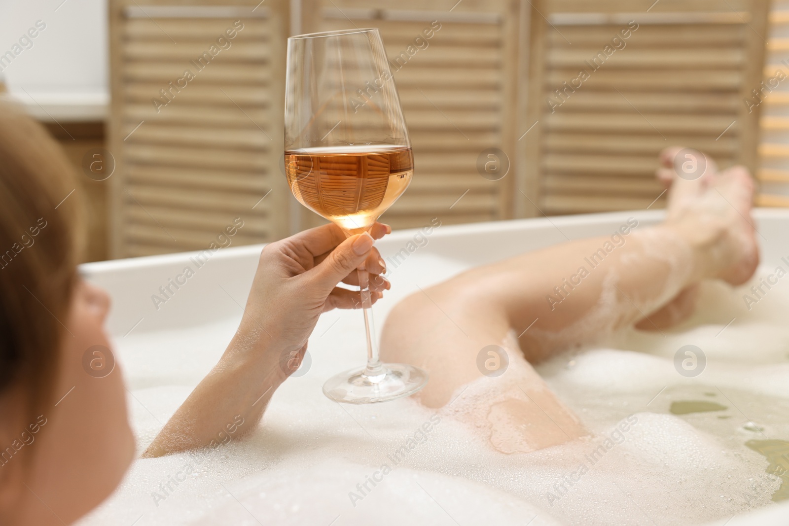 Photo of Woman with glass of wine taking bath in tub indoors, closeup