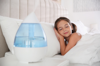 Photo of Cute little girl sleeping in bedroom with modern air humidifier