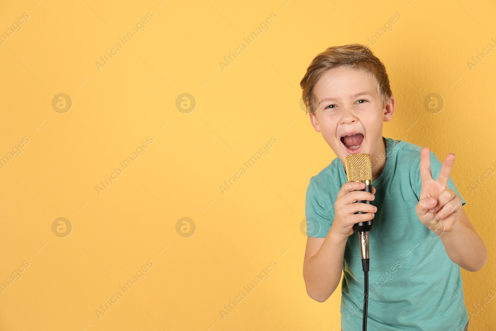 Photo of Cute boy singing in microphone on color background. Space for text