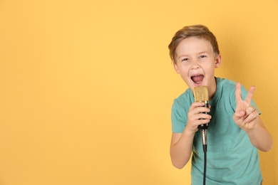 Photo of Cute boy singing in microphone on color background. Space for text