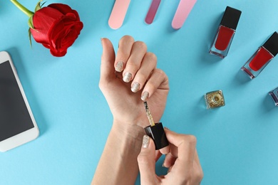 Photo of Woman applying nail polish on color background, top view