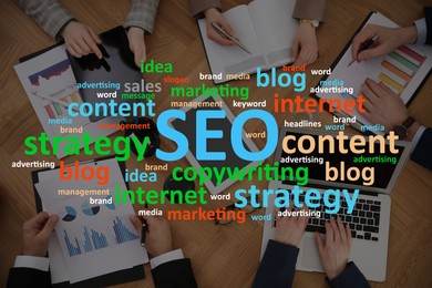Image of Search engine optimization (SEO). Cloud of words above marketing team developing strategy of internet promotion at wooden table, top view