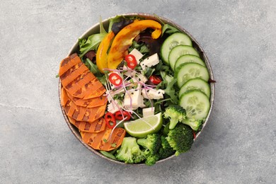 Photo of Bowl with many different vegetables and tofu on grey table, top view. Vegan diet