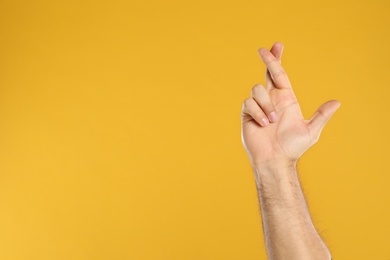 Photo of Man with crossed fingers and space for text on yellow background, closeup. Superstition concept