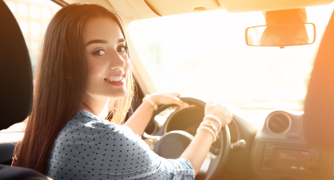 Image of Happy young woman sitting in modern car on sunny day