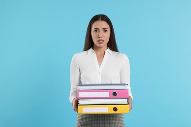 Disappointed woman with folders on light blue background