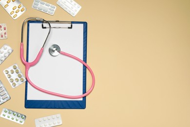 Photo of Stethoscope, clipboard and pills on beige background, flat lay. Space for text