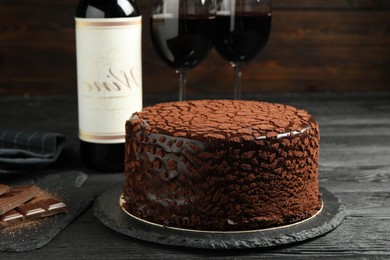 Photo of Delicious truffle cake, chocolate pieces and red wine on black wooden table