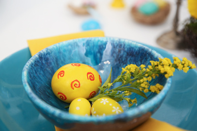 Photo of Easter eggs and mimosa flower in bowl, closeup. Festive table setting