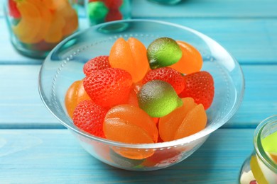 Photo of Delicious gummy fruit shaped candies in glass bowl on light blue wooden table, closeup