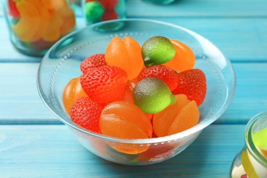 Delicious gummy fruit shaped candies in glass bowl on light blue wooden table, closeup