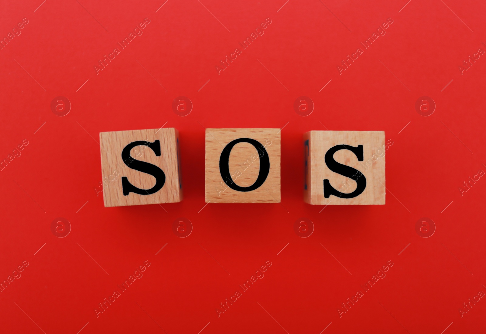 Photo of Abbreviation SOS made of wooden cubes on red background, top view