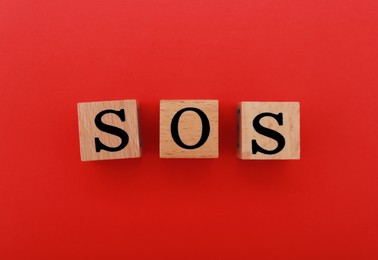 Photo of Abbreviation SOS made of wooden cubes on red background, top view