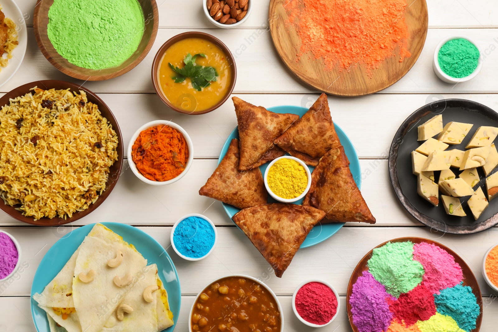 Photo of Traditional Indian food and color powders on white wooden table, flat lay. Holi festival celebration