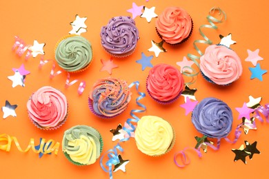 Photo of Delicious cupcakes with bright cream and party decor on orange background, flat lay