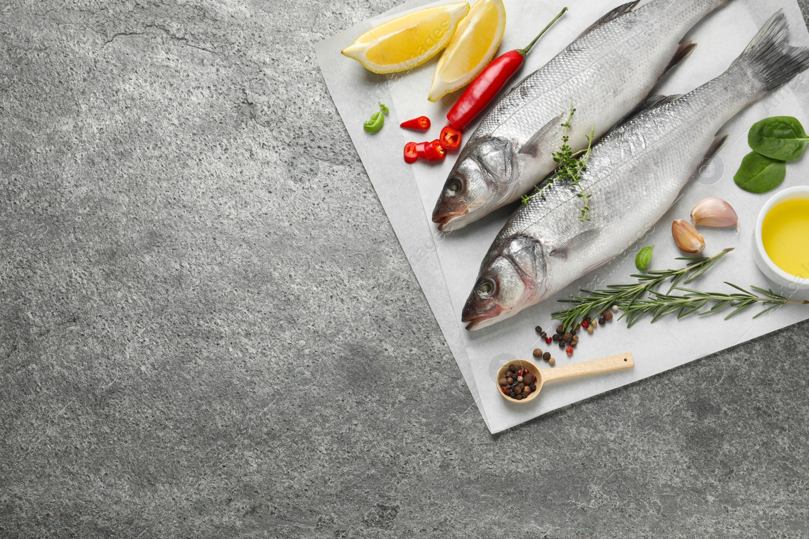 Photo of Sea bass fish and ingredients on grey table, top view. Space for text