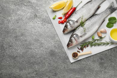 Sea bass fish and ingredients on grey table, top view. Space for text
