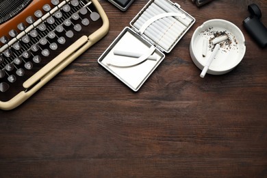 Photo of Open case with tobacco filter cigarettes, lighter and ashtray near vintage typewriter, flat lay. Space for text