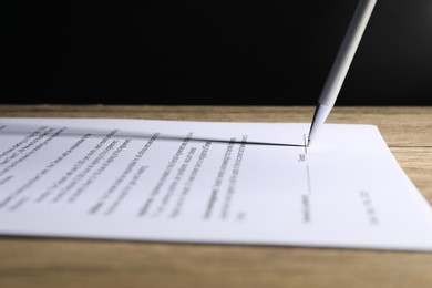 Photo of Signing document with pen on wooden table, closeup
