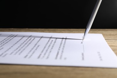 Signing document with pen on wooden table, closeup