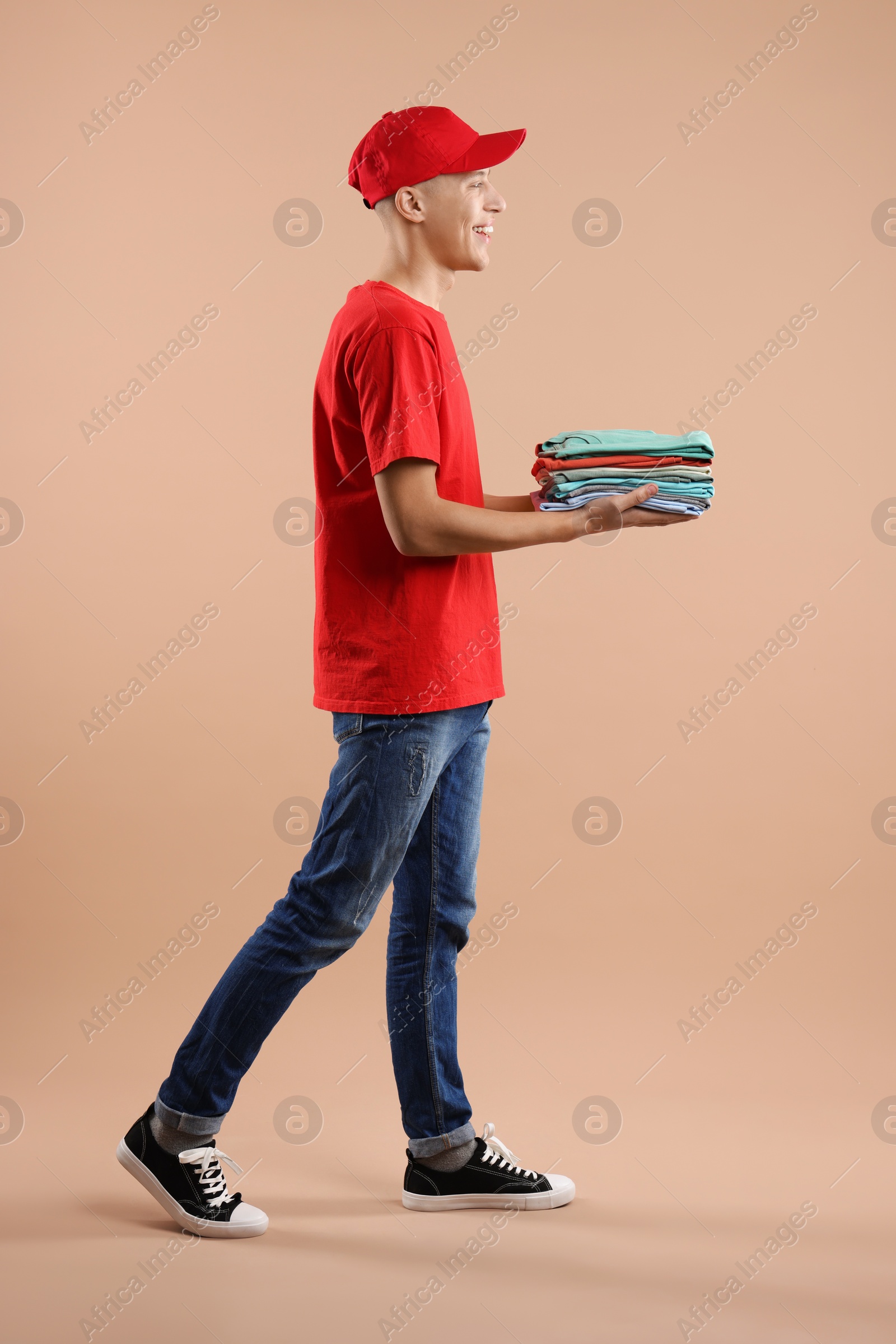 Photo of Dry-cleaning delivery. Happy courier holding folded clothes on beige background