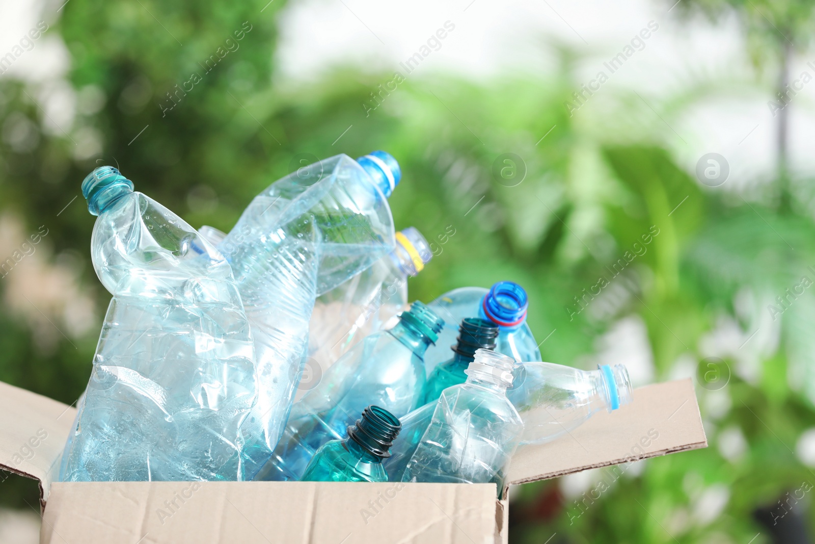 Photo of Cardboard box with used plastic bottles and space for text on blurred background. Recycling problem