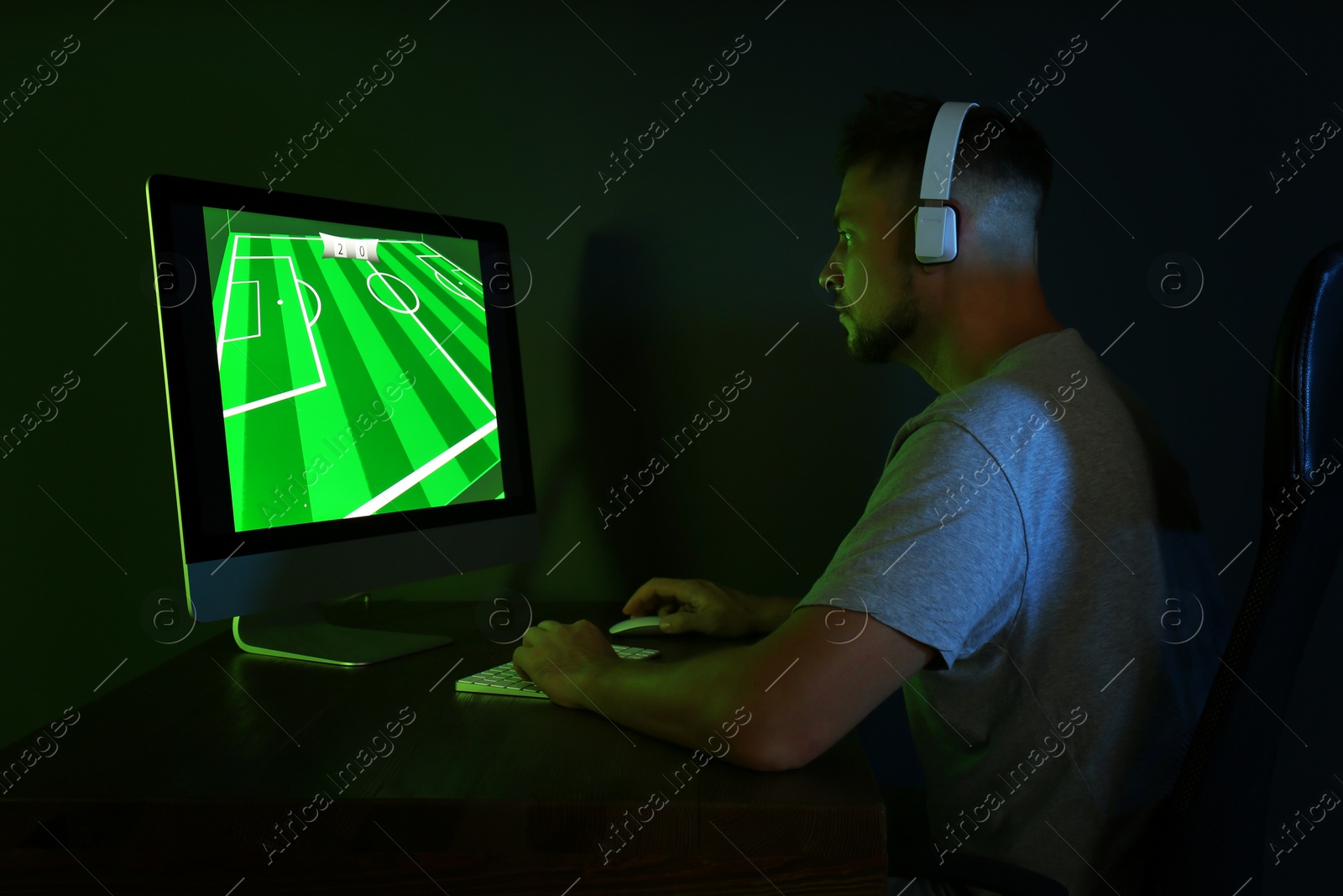 Photo of Man with headphones playing video game on modern computer in dark room