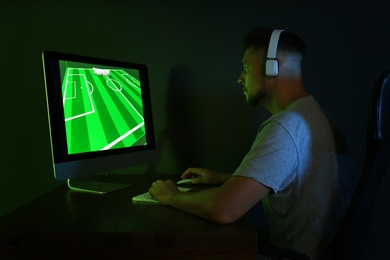 Photo of Man with headphones playing video game on modern computer in dark room